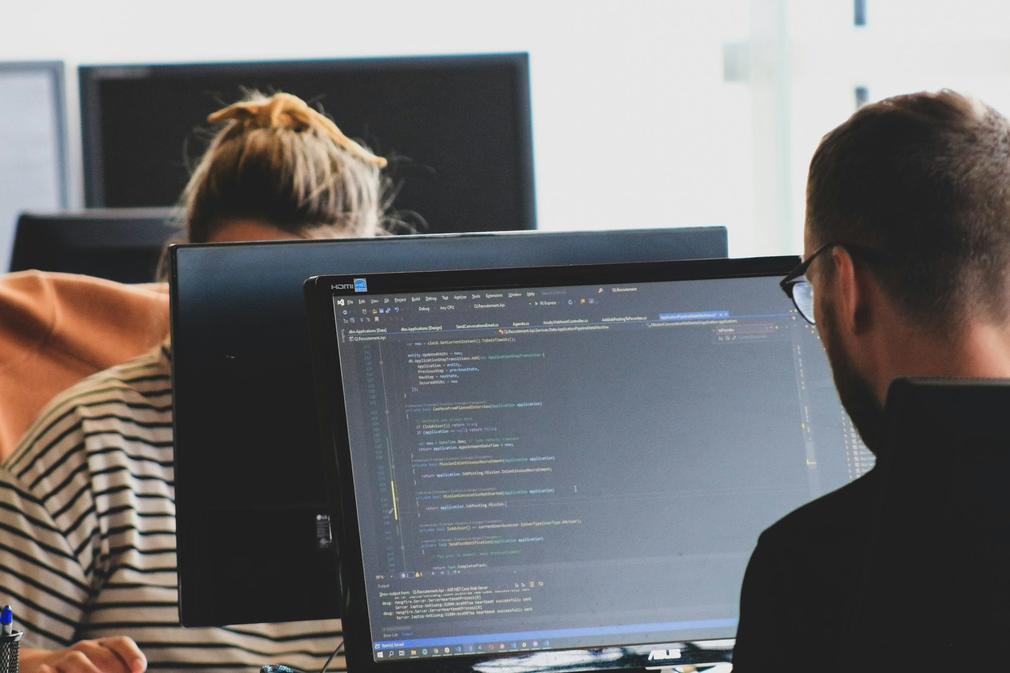 Two analysts reviewing code and data across multiple monitors